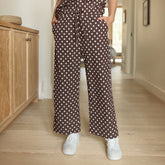 Close up of woman wearing brown polka dot pants—cutest cropped, wide-leg pants—standing in a hallway.