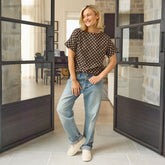 Woman in Albion's best-selling shirt in brown polka dot print with jeans standing in a modern interior setting.