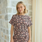Woman wearing a floral, elevated t-shirt standing against a stone wall.