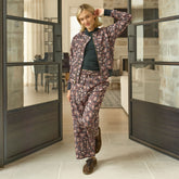 Woman standing against large glass doors wearing a cute matching outfit—neutral floral bomber jacket with brown floral cropped pants. 