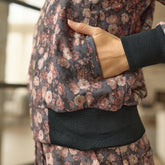 Close up detail of the pocket of a brown, floral women's bomber jacket with visible Albion logo and a hand in the pocket. 