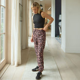 Woman in black tank top and neutral jogger pants standing in a well-lit room with large windows.