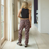 Back view of woman wearing a cropped black tank top with neutral floral women's jogger pants and sneakers, standing in a hallway.