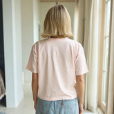 Back view of woman wearing a light pink, boxy women's tee and denim skirt.