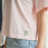 Close up of woman wearing a light pink t-shirt with an Albion brand label with a blurred background