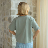 Back view of woman wearing a light green t-shirt that's perfectly cropped and boy, standing against a stone wall.