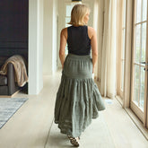 Woman in a long green skirt walking through a modern living room.