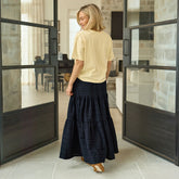 Woman in a yellow top and black skirt standing in a modern interior setting with large glass doors.