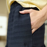 Woman wearing a black textured skirt with a yellow top, hand in pocket.