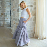 Woman wearing a white top and light blue skirt standing in a room with stone walls and a curtain.