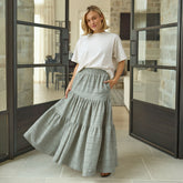 Woman wearing a white top and taupe skirt standing in a room with large glass doors.