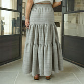 Woman wearing a long maxi skirt in  taupe in a room with large windows.