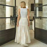 Woman in a white maxi skirt standing in a modern interior setting with glass doors.