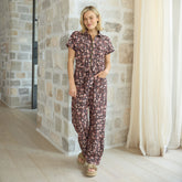 Woman wearing a flattering jumpsuit standing in a room with stone walls and white curtains.