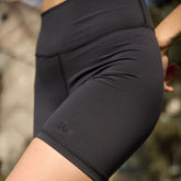 Close-up of a person wearing black high-waisted athletic shorts, showing the side hip and thigh with a small tonal logo near the hem.