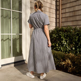 Back view of woman in a navy gingham dress standing outside a building with greenery.
