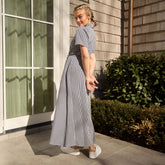Woman in a short-sleeved maxi dress in navy gingham standing outside with greenery in the background