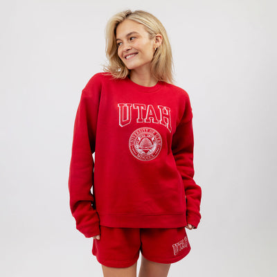 Person wearing a red 'UTAH' sweatshirt and shorts on a white background