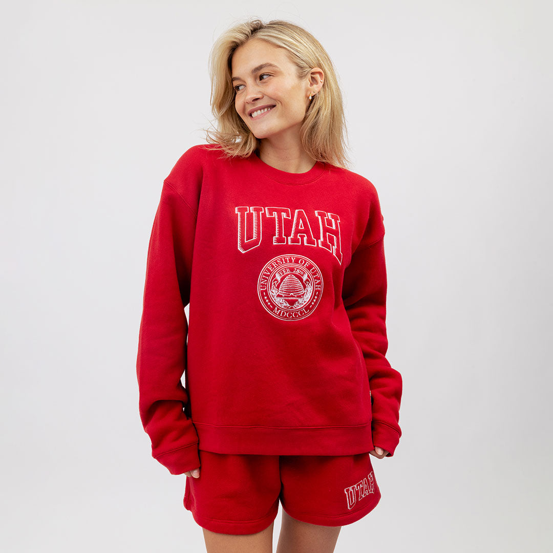 Person wearing a red 'UTAH' sweatshirt and shorts on a white background