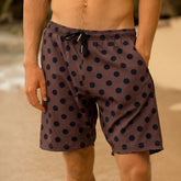 Man wearing brown and black polka dot swim trunks for men on a blurred beach background