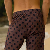 Close up back view of man wearing men's swimsuit in brown and black polka dot print on a blurred ocean background