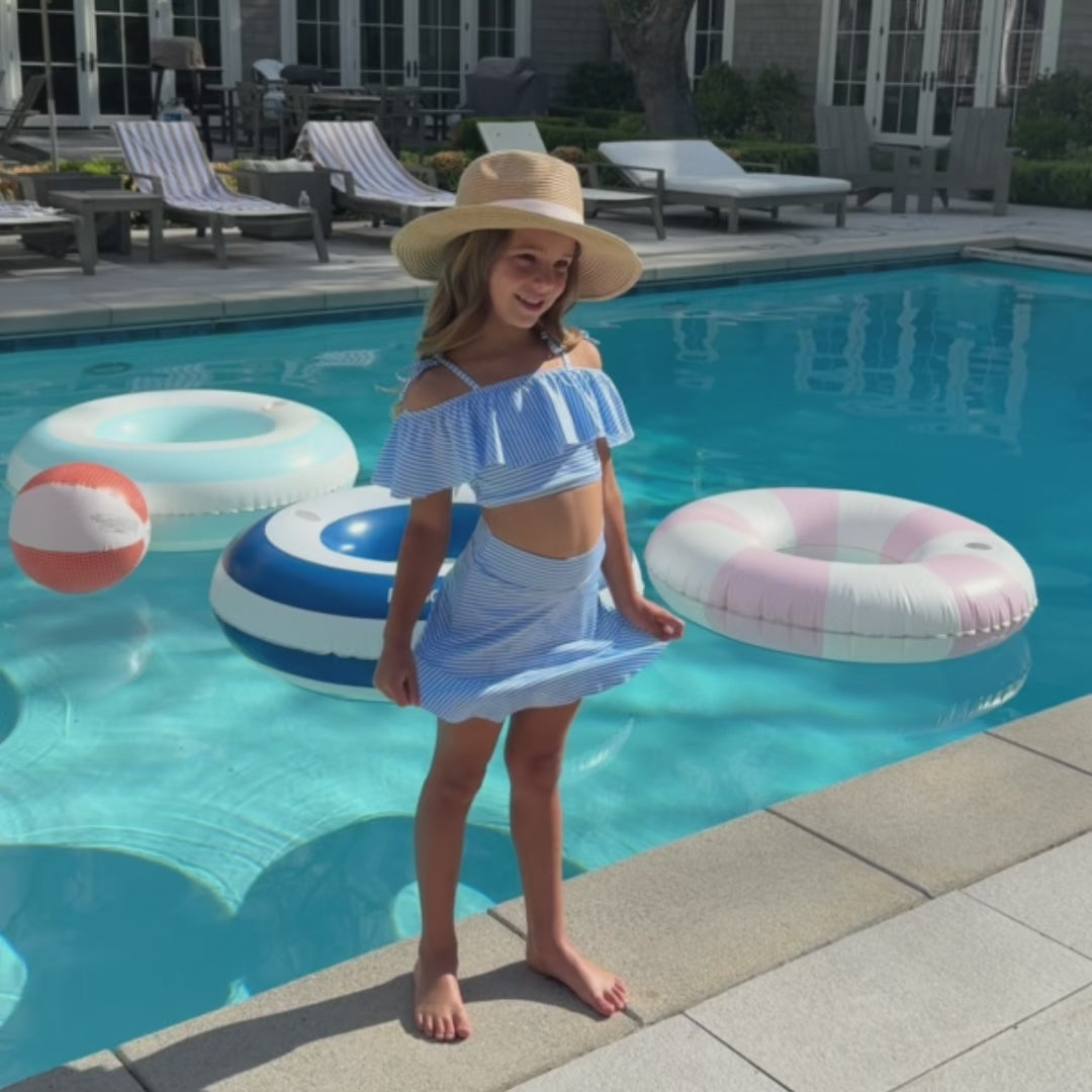 Video of girl in kid's two piece swimsuit with swim skirt standing in front of a pool with pool floaties.