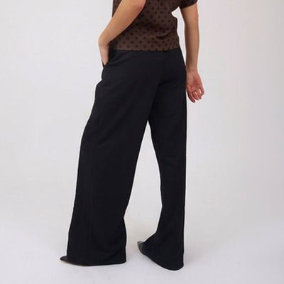 Side view of woman wearing black, women's wide-leg pants and a brown polka dot top on a white background