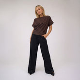 Woman wearing a brown polka dot top and black wide-leg trousers on a white background