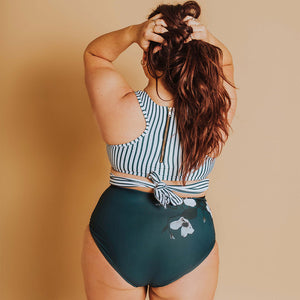 woman showing the back of her one-piece swimsuit in a green and white with floral pattern