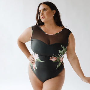 woman wearing a black and floral design one-piece swimsuit holding her hand on her hip