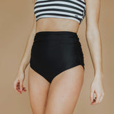 woman wearing high waisted ruched black swim bottoms in a close up view