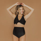 Model posing wearing black two piece swimsuit with top knot