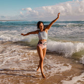 woman standing in the ocean wearing a two-piece swimsuit with green and white stripes and a floral pattern