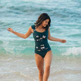 woman wearing a dark green and pink floral pattern one-piece swimsuit