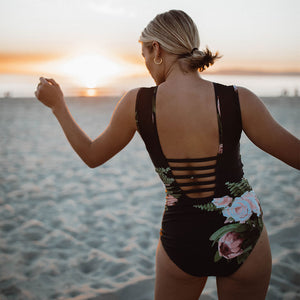 woman showing the back of her black one-piece swimsuit with pink flowers