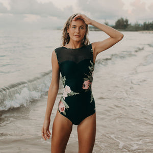 woman standing at the beach wearing a black swimsuit with a floral design