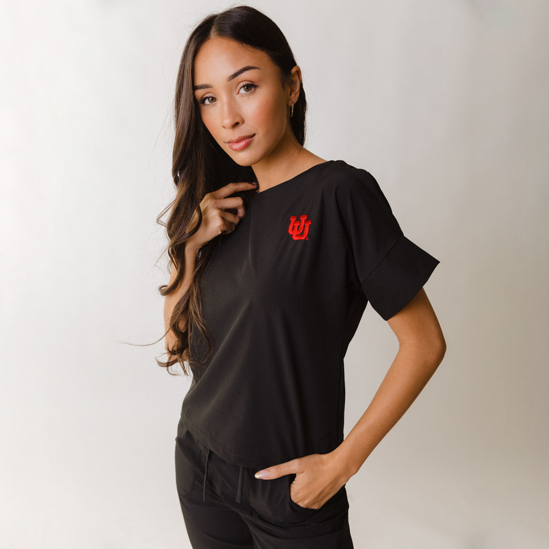 A woman modeling a black t-shirt with the University of Utah logo on the upper left chest area.