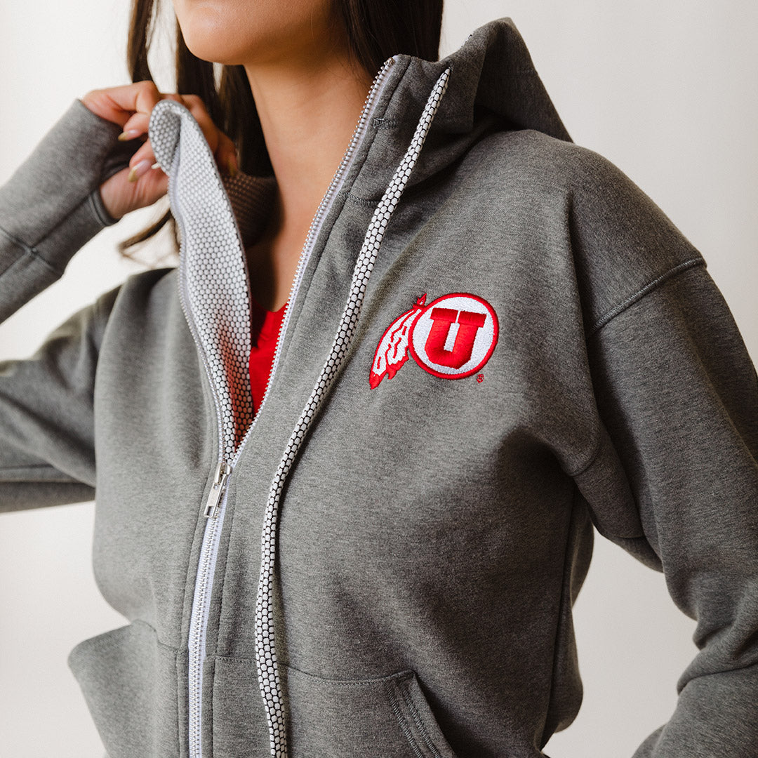A woman wearing a gray zip-up hoodie with the University of Utah logo in red on the left chest area.